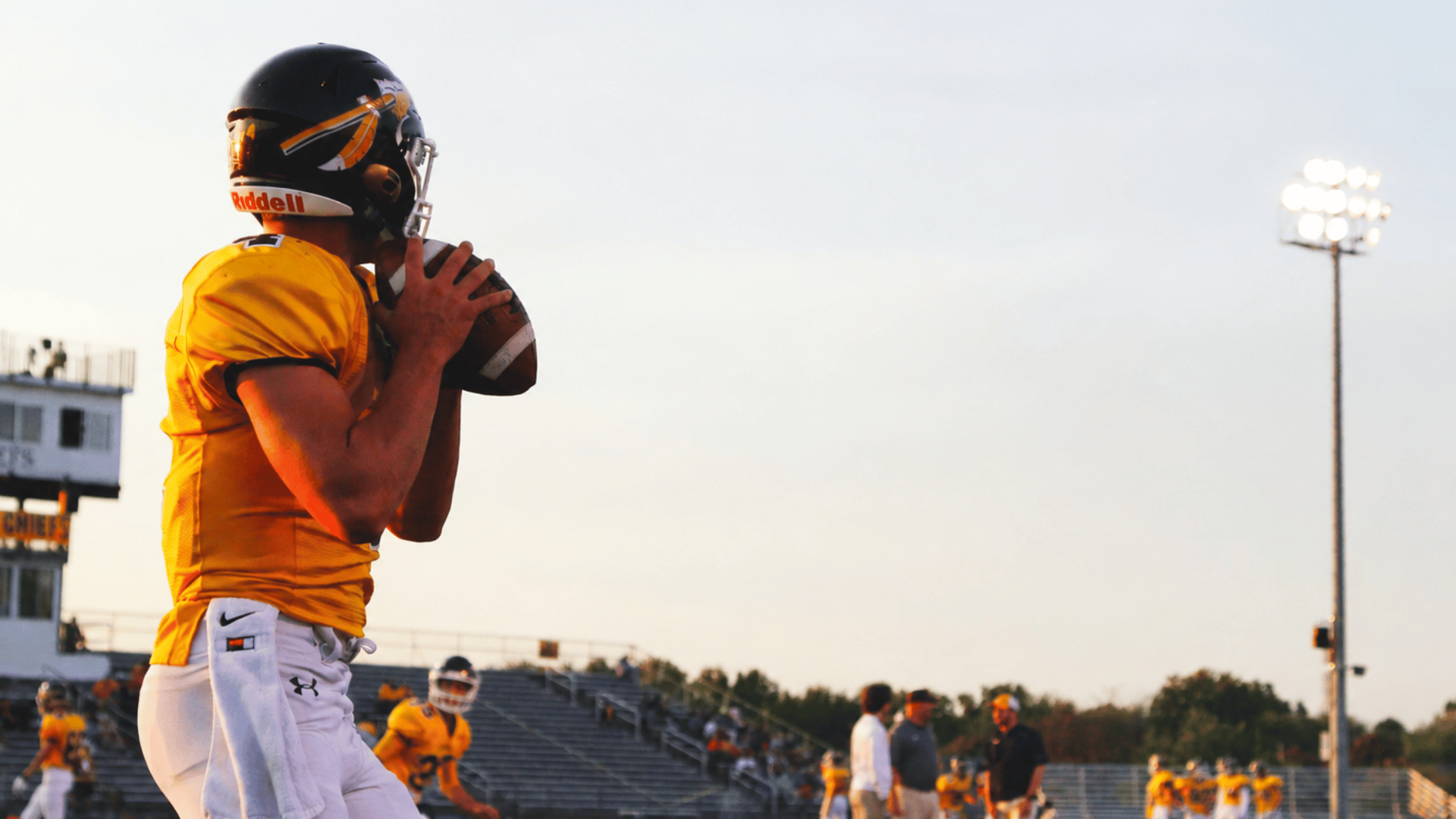 american football quarterback holds the ball before a play during warmups on a stadium field at sunset