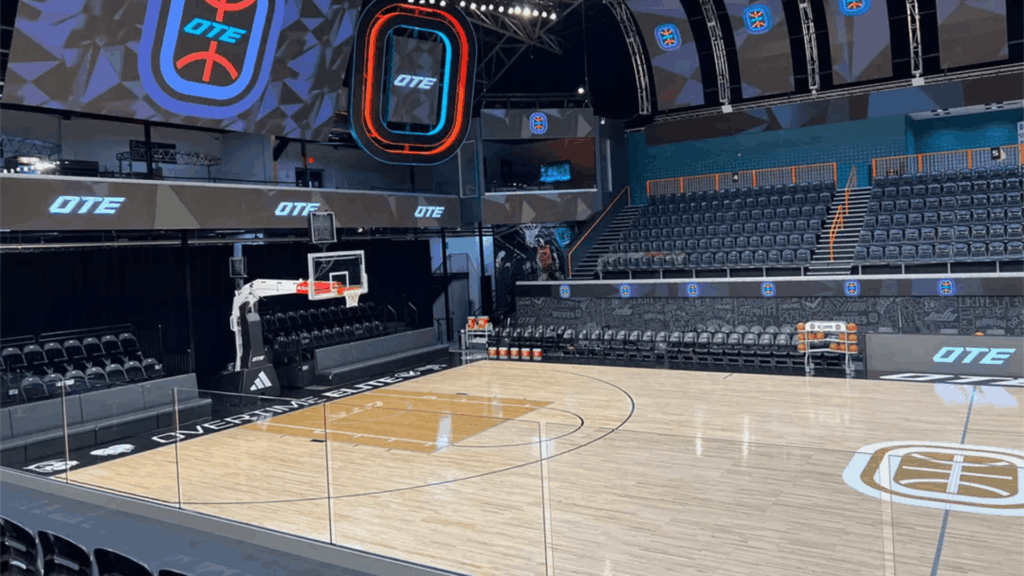 an empty indoor basketball arena with an ote court digital screens overhead lighting and rows of dark seats