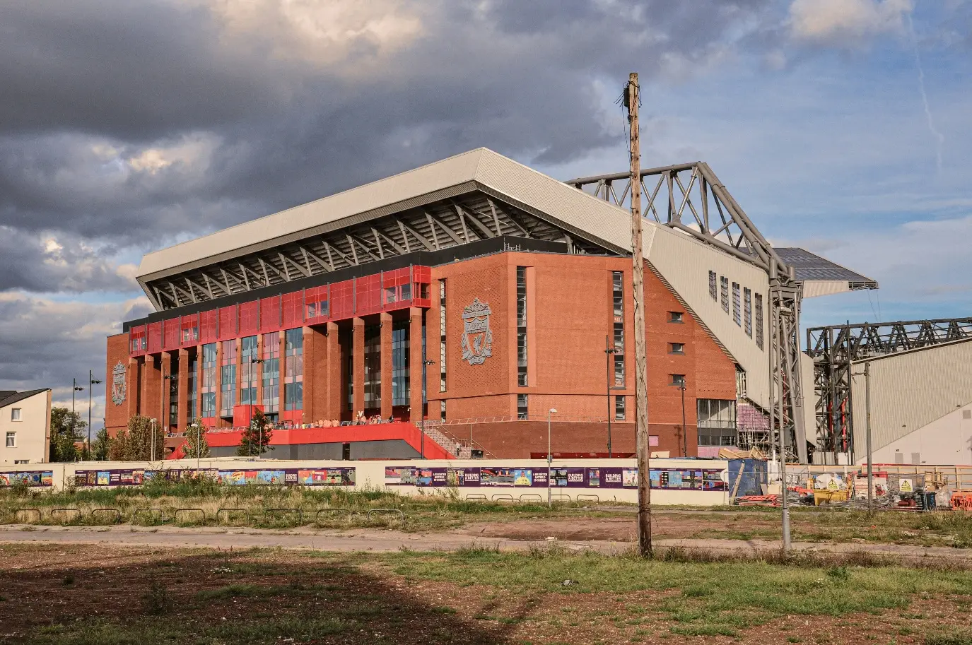 Stadium with red brick facade and large emblem under cloudy sky in urban setting