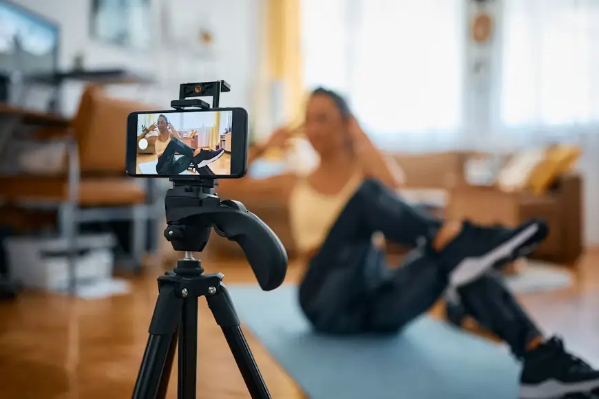 Smartphone on tripod recording woman exercising on yoga mat in cozy living room