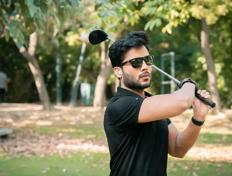 Golfer in black shirt swinging club on lush green golf course under bright sunlight