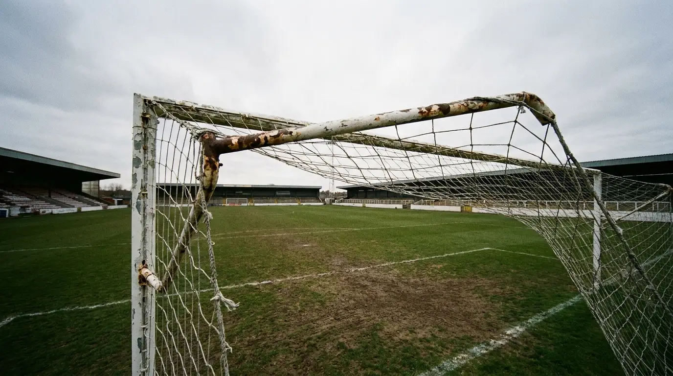 Rusty soccer goalpost on an empty grass field under cloudy sky