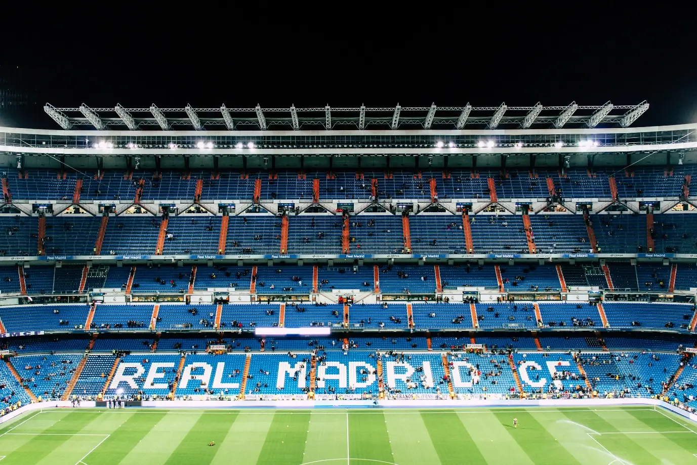 Empty stadium seats with "Real Madrid C.F." visible on blue stands at night