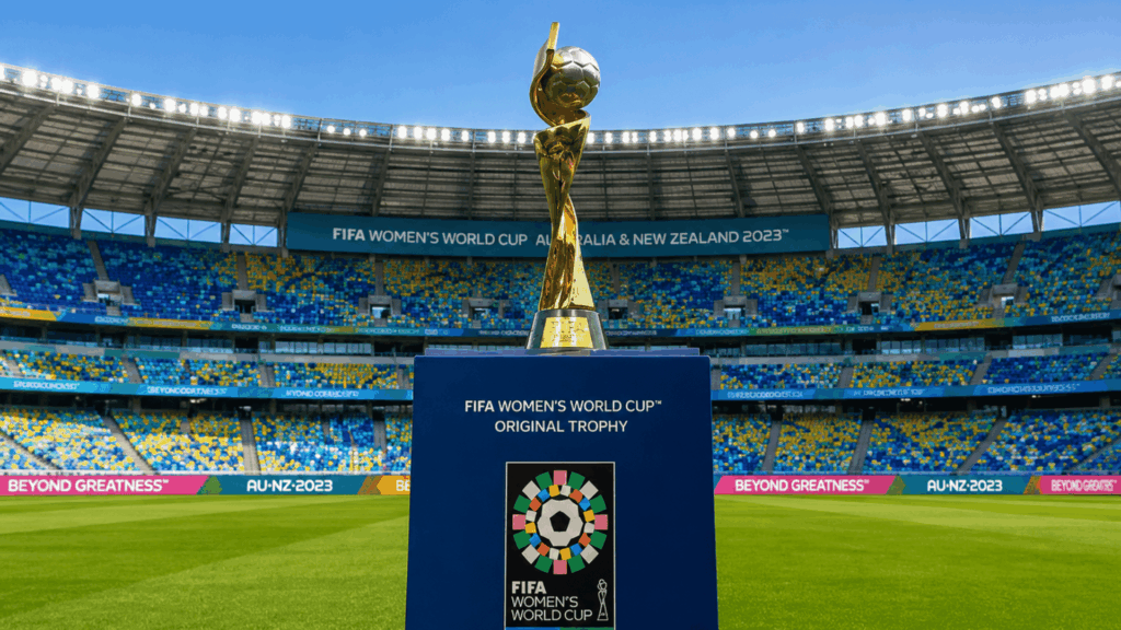 fifa womens world cup trophy displayed on a dark blue podium inside a modern football stadium