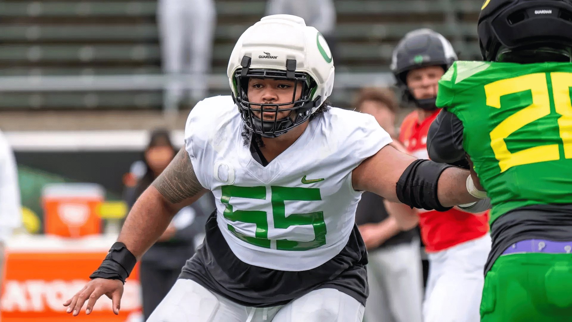 football lineman in a white and green uniform blocks an opponent during a game near the sideline