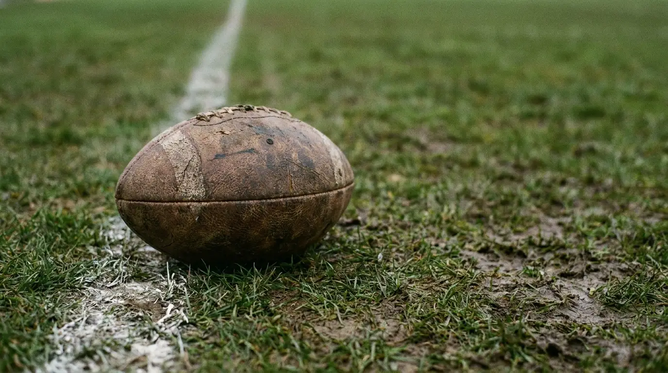 Worn rugby ball resting on muddy grass field with white line marking