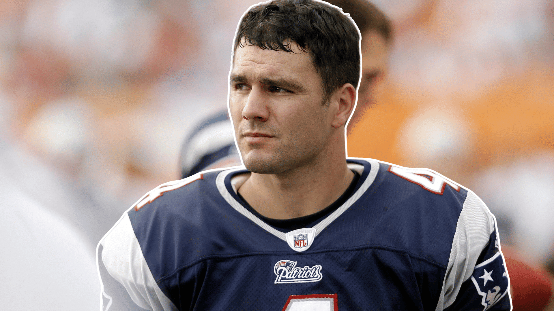 football player in a navy jersey stands on the sideline looking to the side before the game with a blurred stadium crowd behind him