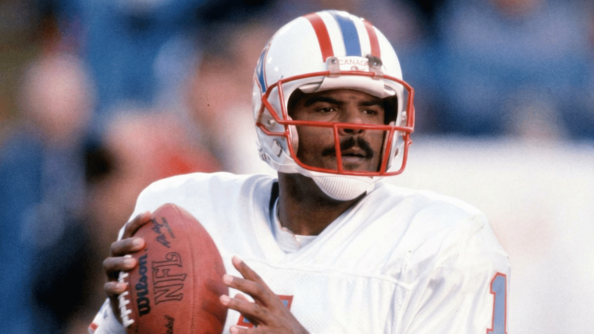football player in a white jersey and helmet holds a football in passing position while looking downfield during the game