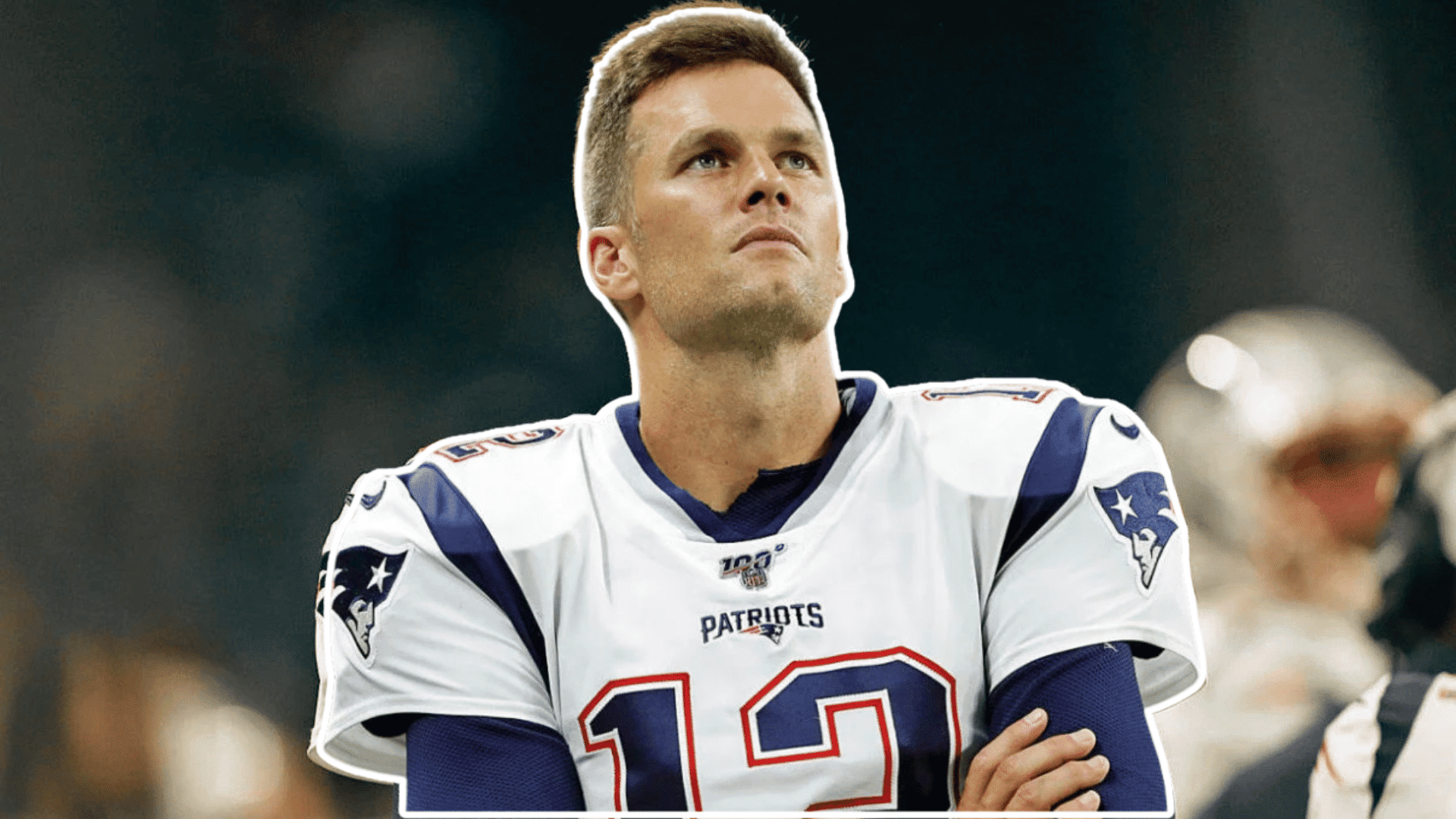 football player in a white jersey stands on the sideline with arms crossed looking upward before the game begins