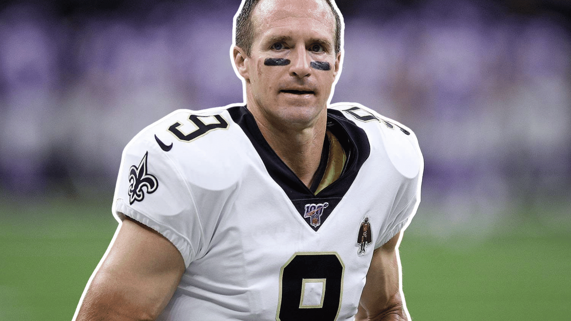 football player in a white jersey with eye black stands on the field before the game with a blurred stadium in the background