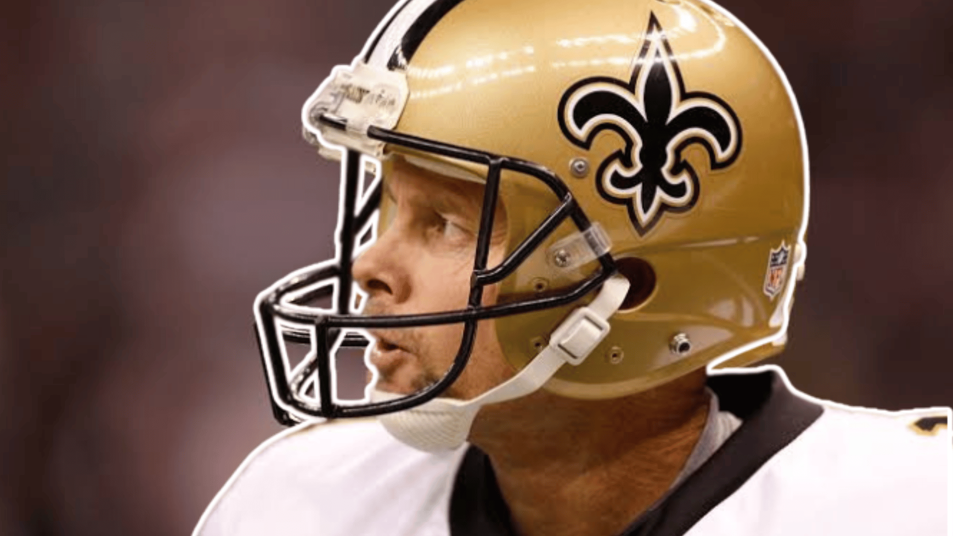 football player wearing a gold helmet and white jersey looks to the side before the game with a blurred stadium in the background