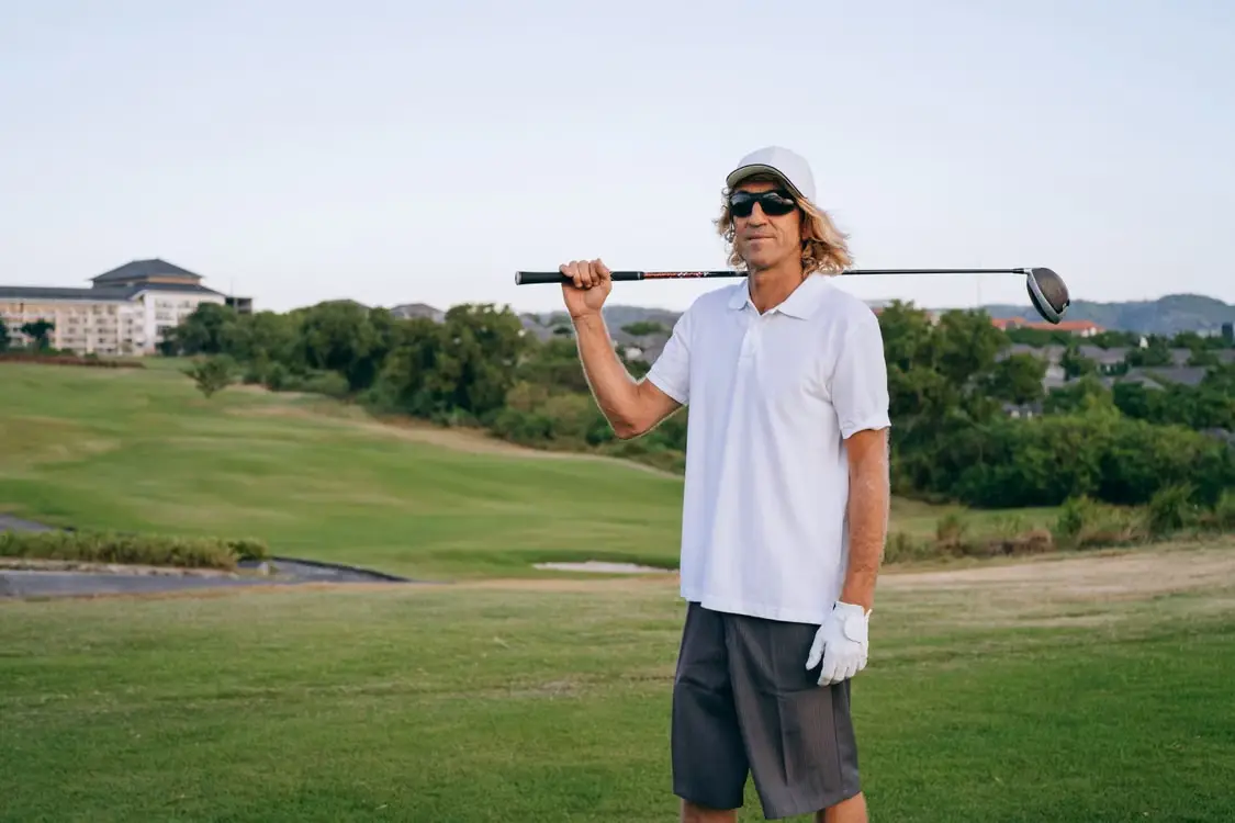 Golfer in white polo holding club on lush green golf course at sunset