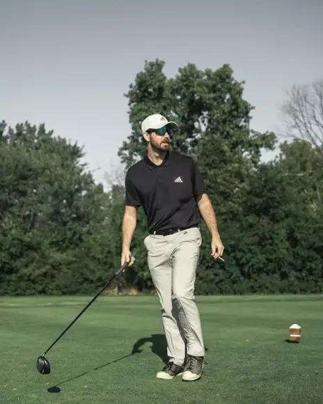 Golfer in black polo and white pants on grassy course under clear sky