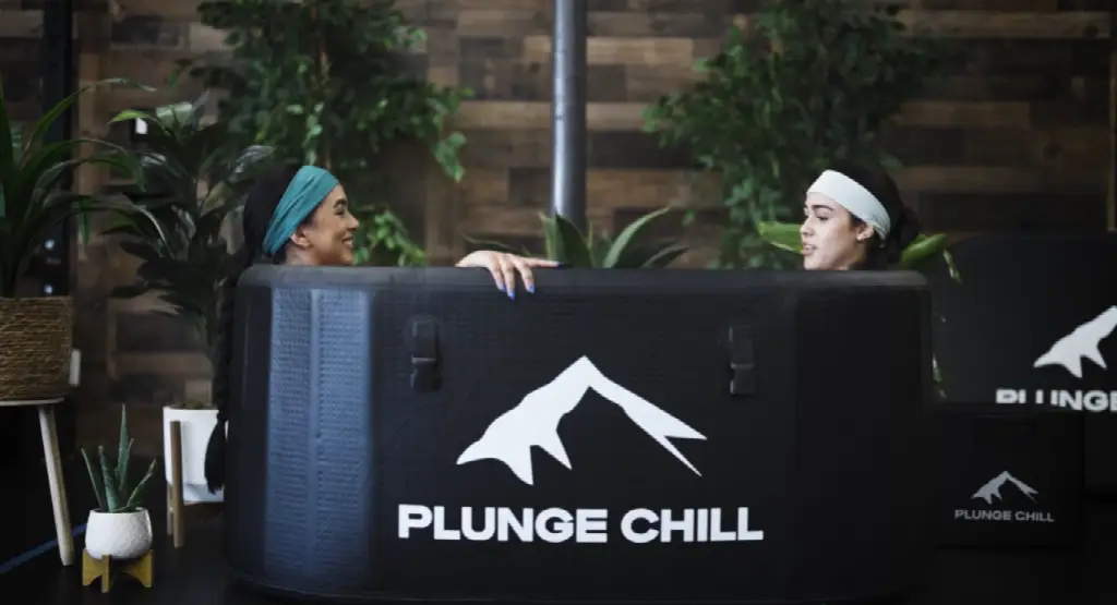 Two women enjoying an ice bath in a plunge tub surrounded by indoor plants