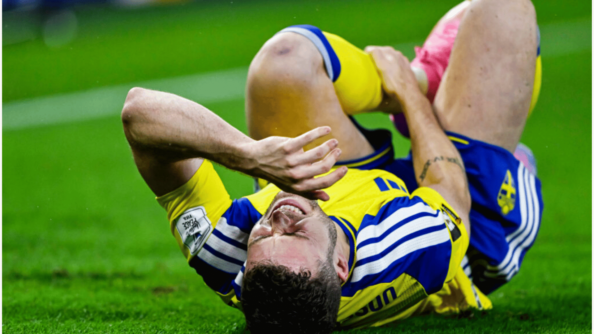 injured soccer player in a yellow and blue uniform lying on the grass in deep pain