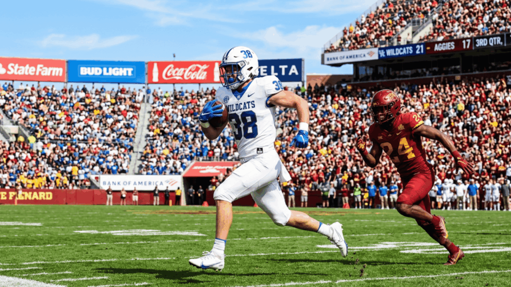 kentucky wildcats player runs with the football ahead of an iowa state defender during a packed stadium game
