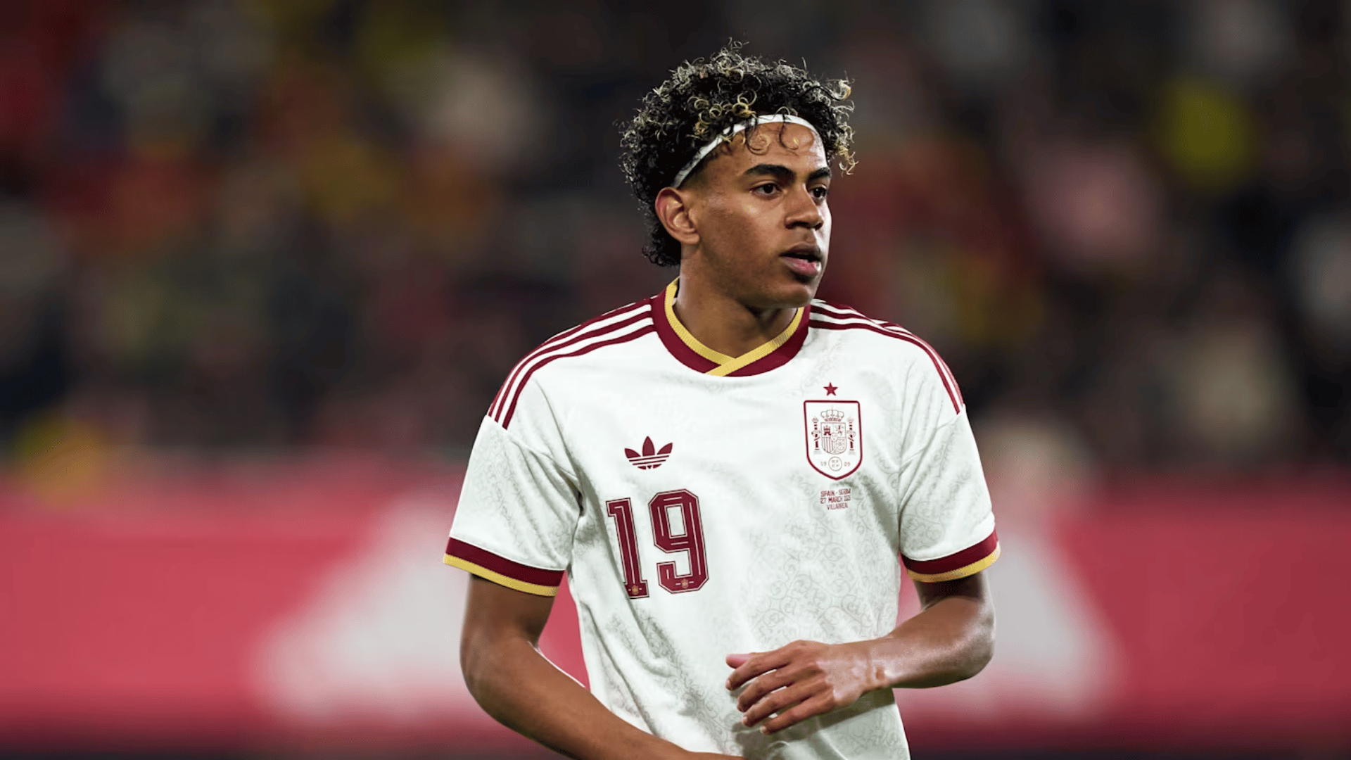 lamine yamal sweating wearing the away spanish fifa jersey looking off with a blurred background