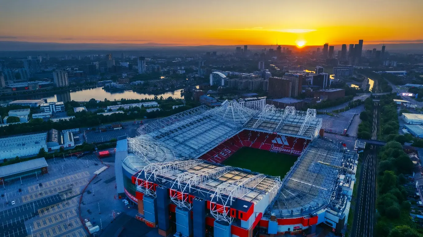Stadium with red seats and roof structure at sunset overlooking cityscape and river