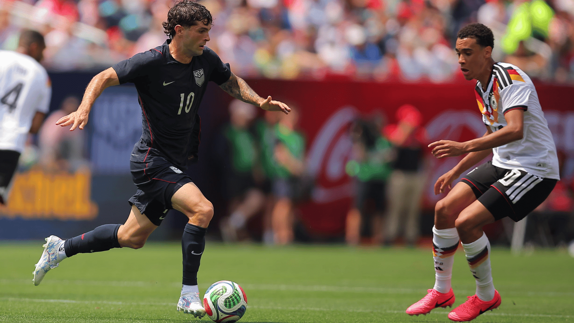 soccer player in dark usa kit dribbles past german defender during a match on a sunny day