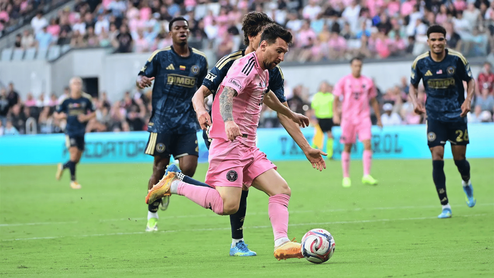 soccer player in pink kit controls the ball while defenders close in during a crowded stadium match