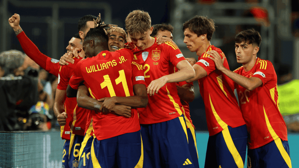 spain players celebrating a goal together on the football field during an international match while wearing the national team kit