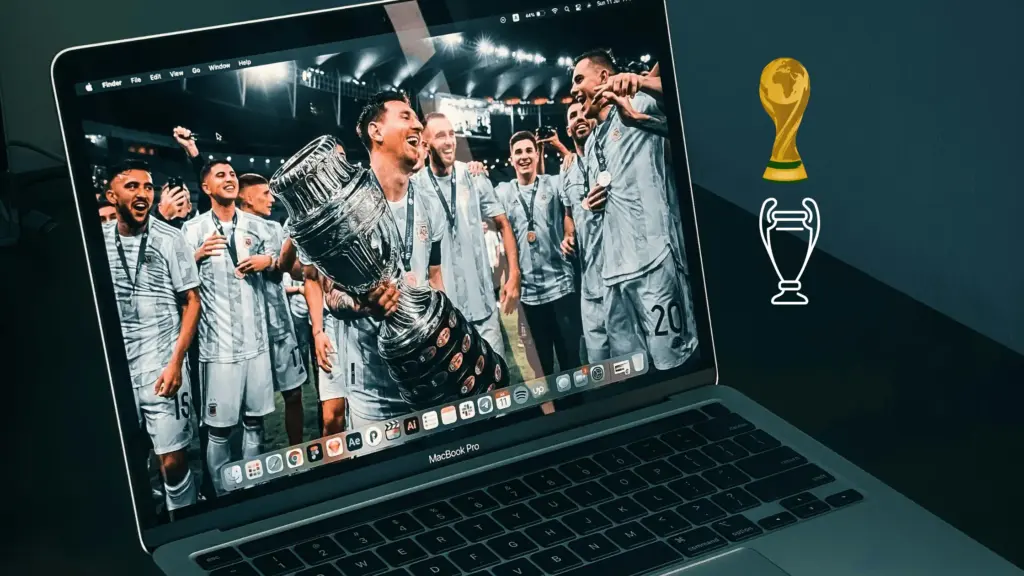 Laptop displaying soccer team celebrating with trophy, on a dark desk with trophy icons nearby