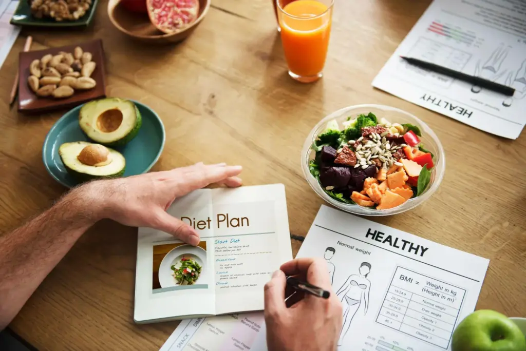 Hands writing in diet plan notebook on wooden table with salad and juice