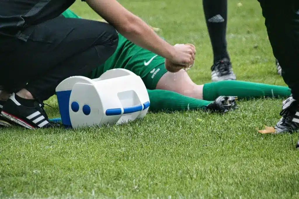 Soccer player receiving medical attention on grassy field with first aid kit nearby