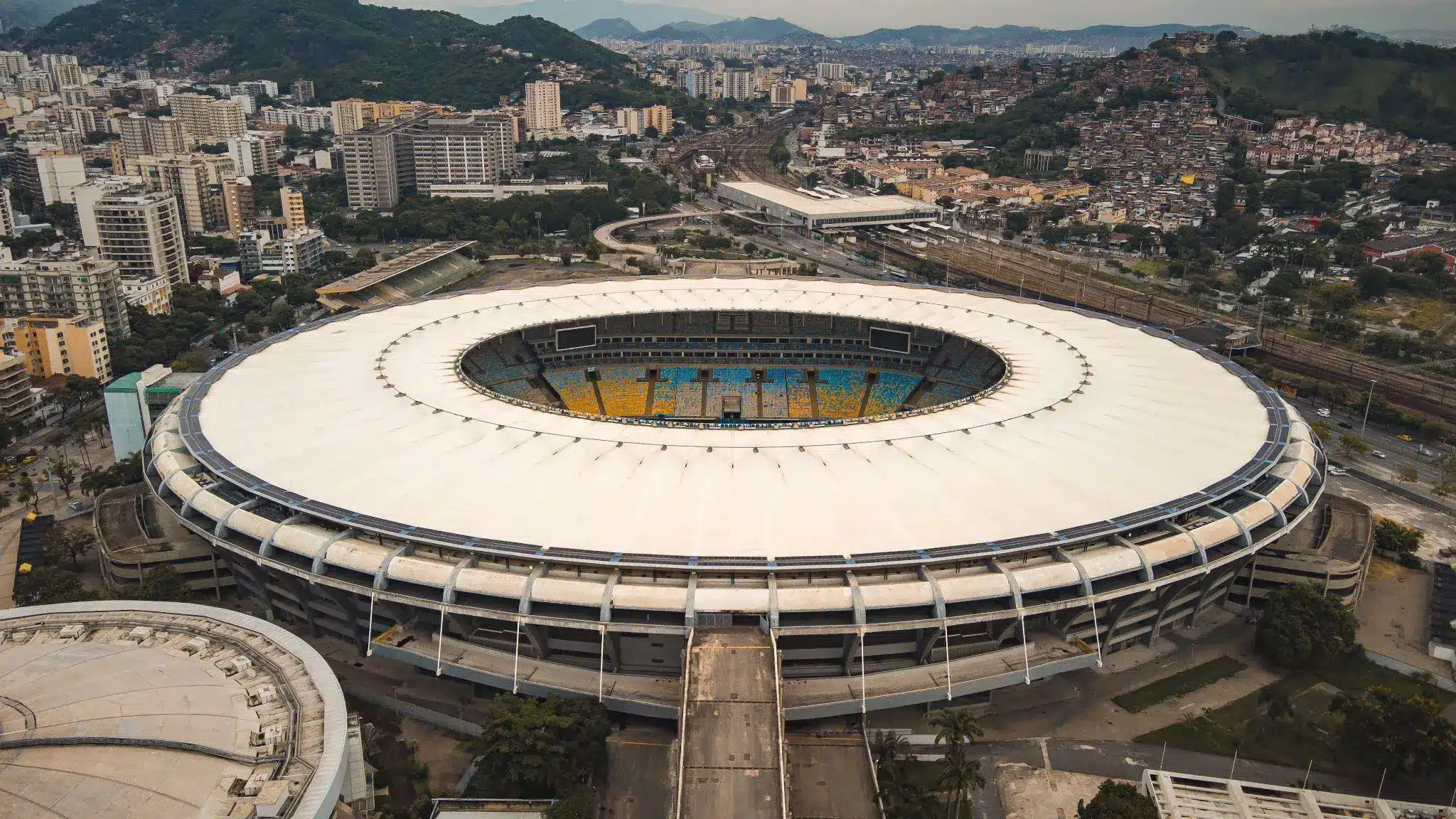 Aerial view of large stadium surrounded by urban cityscape and distant hills