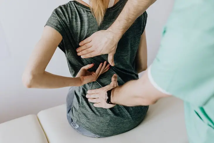 Physical therapist assessing woman's back pain on clinic table