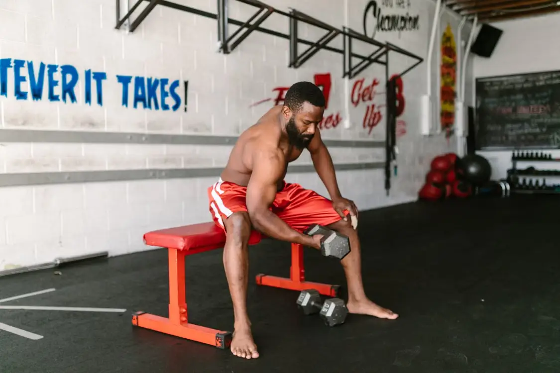 Man performing dumbbell curls on red bench in gym with motivational wall art
