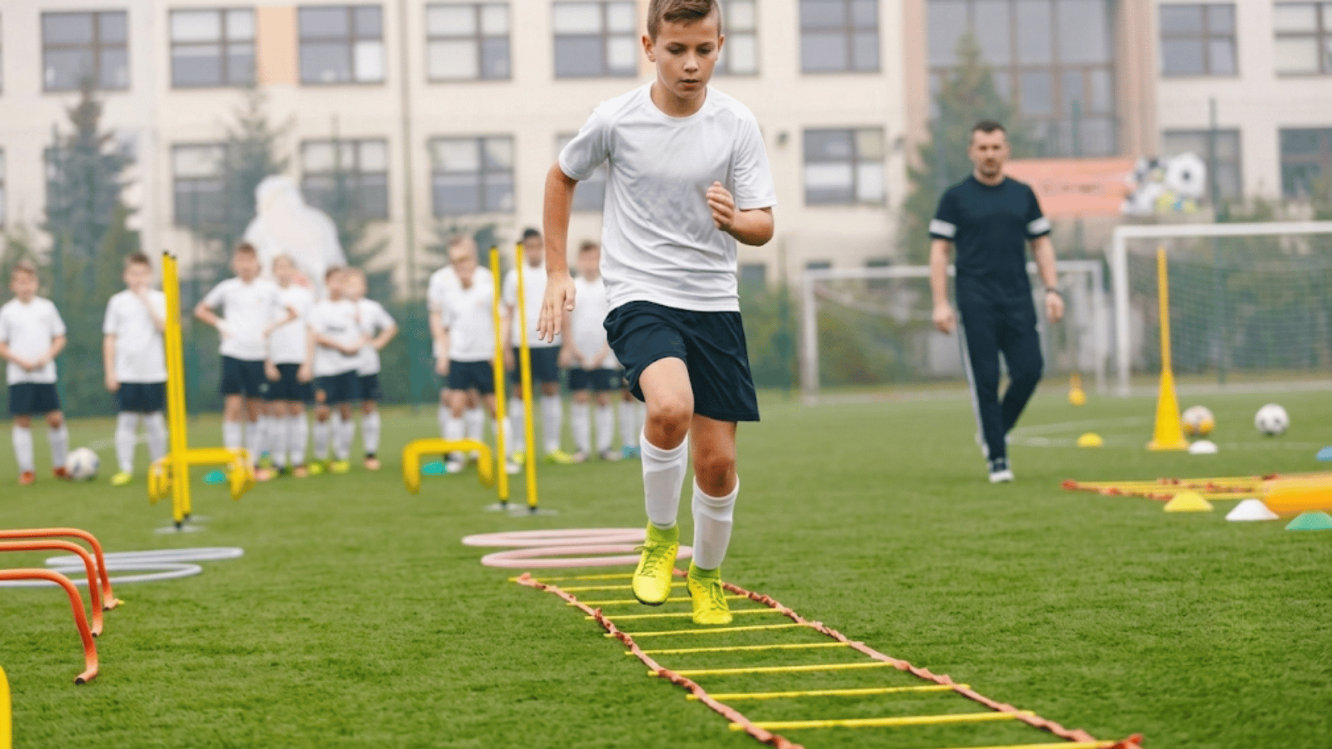 young soccer player completing an agility ladder drill while teammates and coach watch during outdoor practice