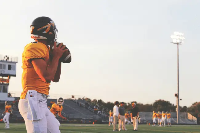 Football player in yellow jersey holding ball on field during practice session with teammates