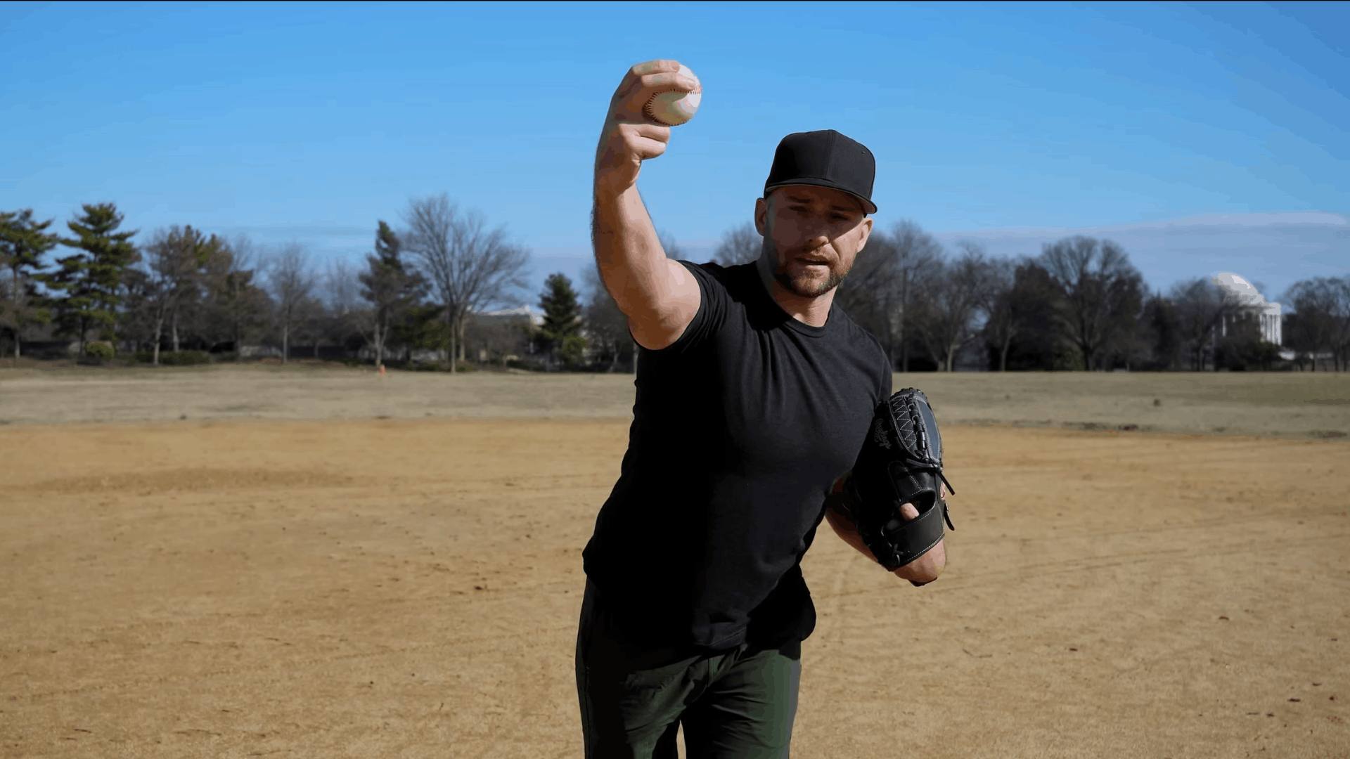 a baseball player demonstrating an overhand throwing motion while holding a glove on a field during a pitching technique lesson (1)