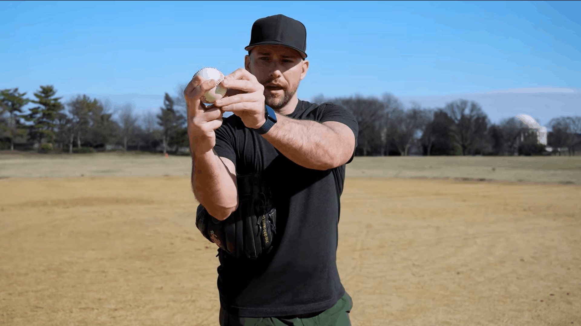 a baseball player demonstrating finger placement on a baseball while standing on a field holding a glove during a pitching lesson (1)