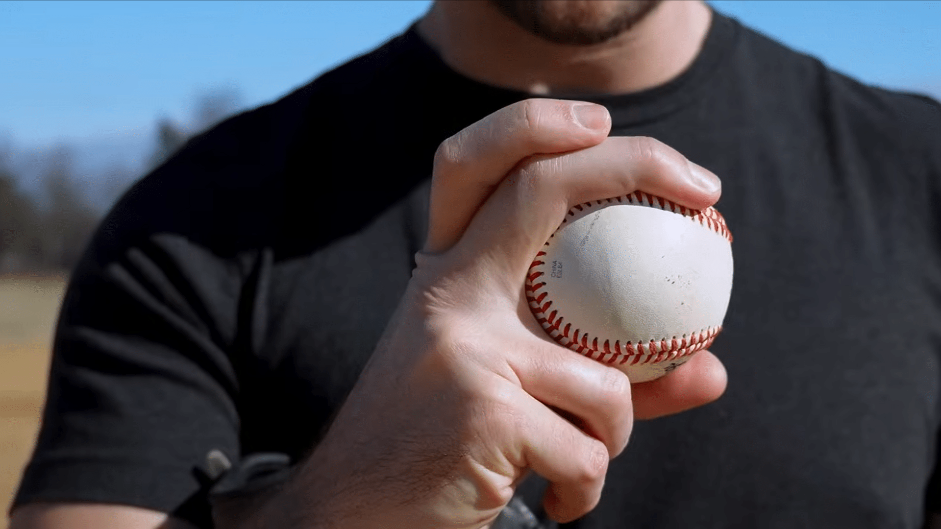 a close up of a hand gripping a baseball with a pitching grip while standing outdoors ready to throw the ball