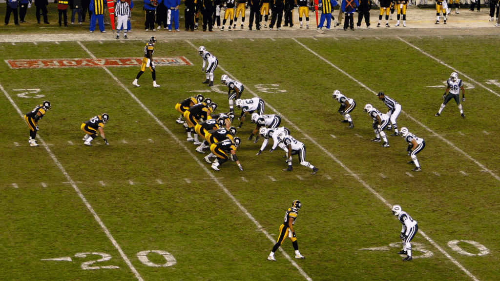 american football teams line up before the snap during a game with players coaches and officials along the sideline