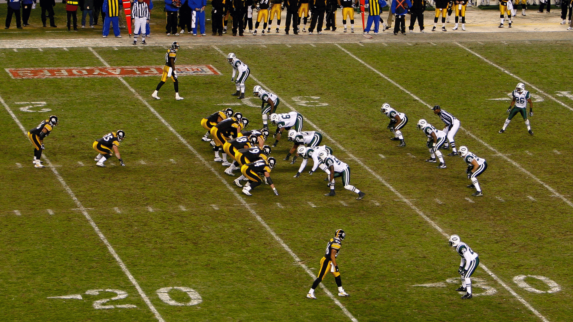 american football teams line up before the snap during a game with players coaches and officials along the sideline