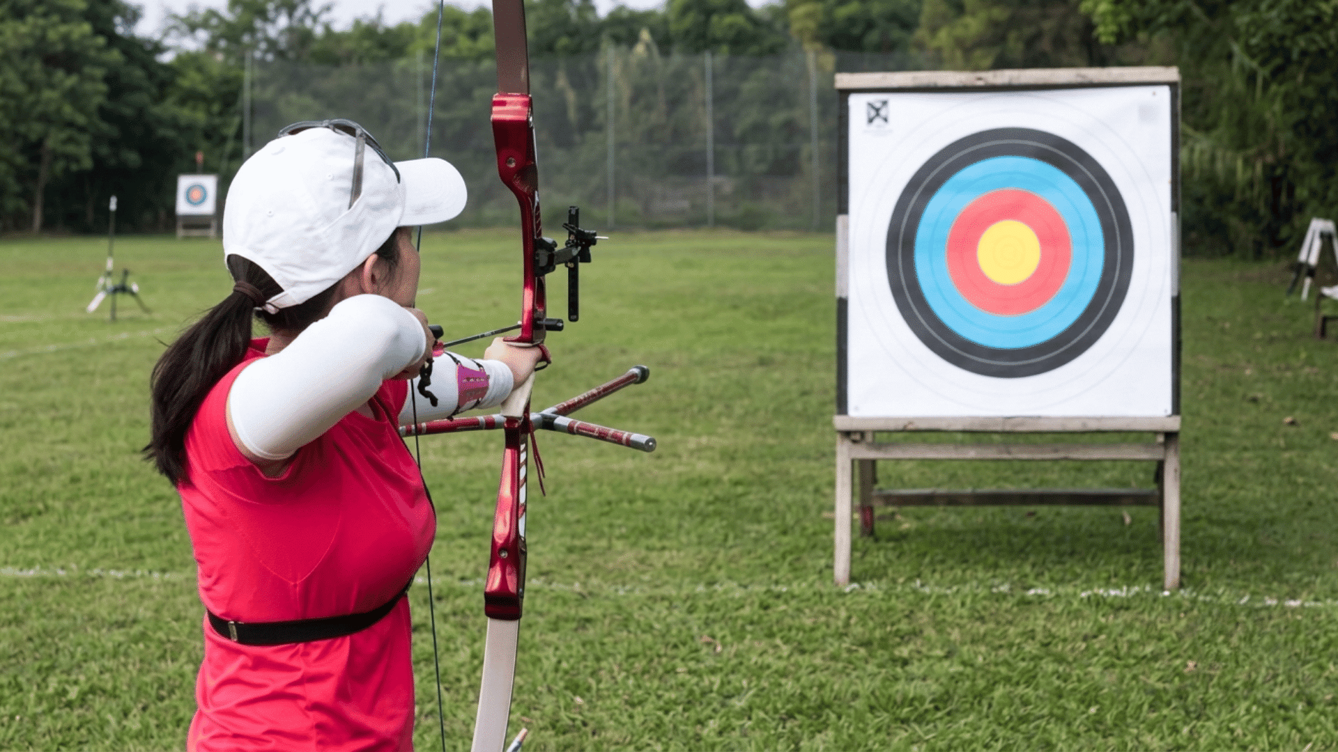 archer aiming a bow at a colorful target on an outdoor range while wearing protective sports equipment (1)