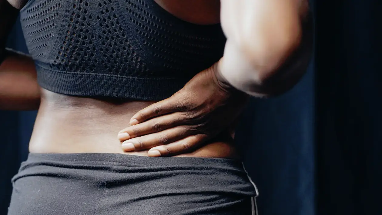 Person in athletic wear holding lower back in dim lighting