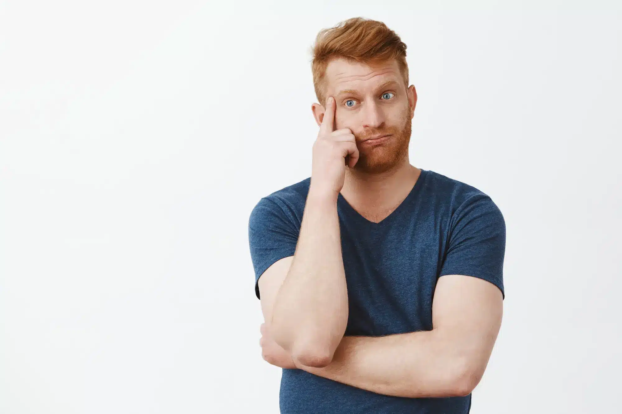 Man with red hair in blue shirt looking thoughtful against plain background