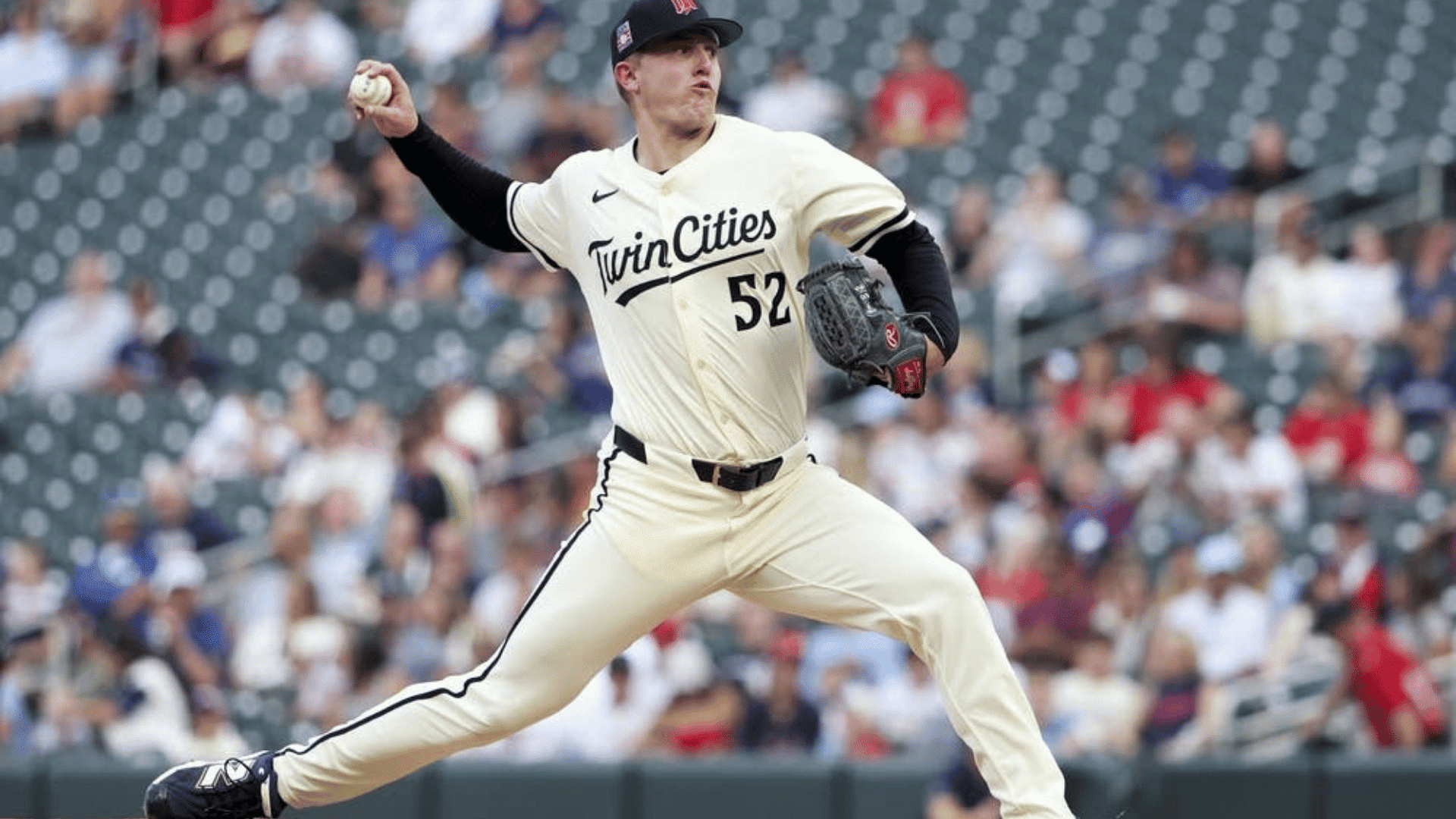 baseball pitcher throwing a pitch during a game while wearing a twin cities uniform with fans watching from the stands