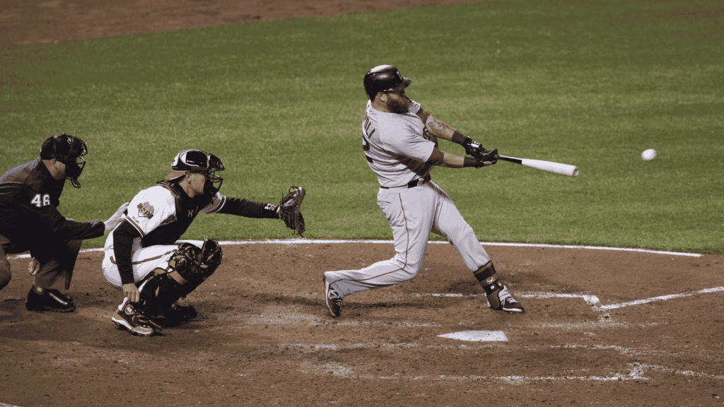 baseball player swings at a pitch while catcher and umpire watch from behind home plate