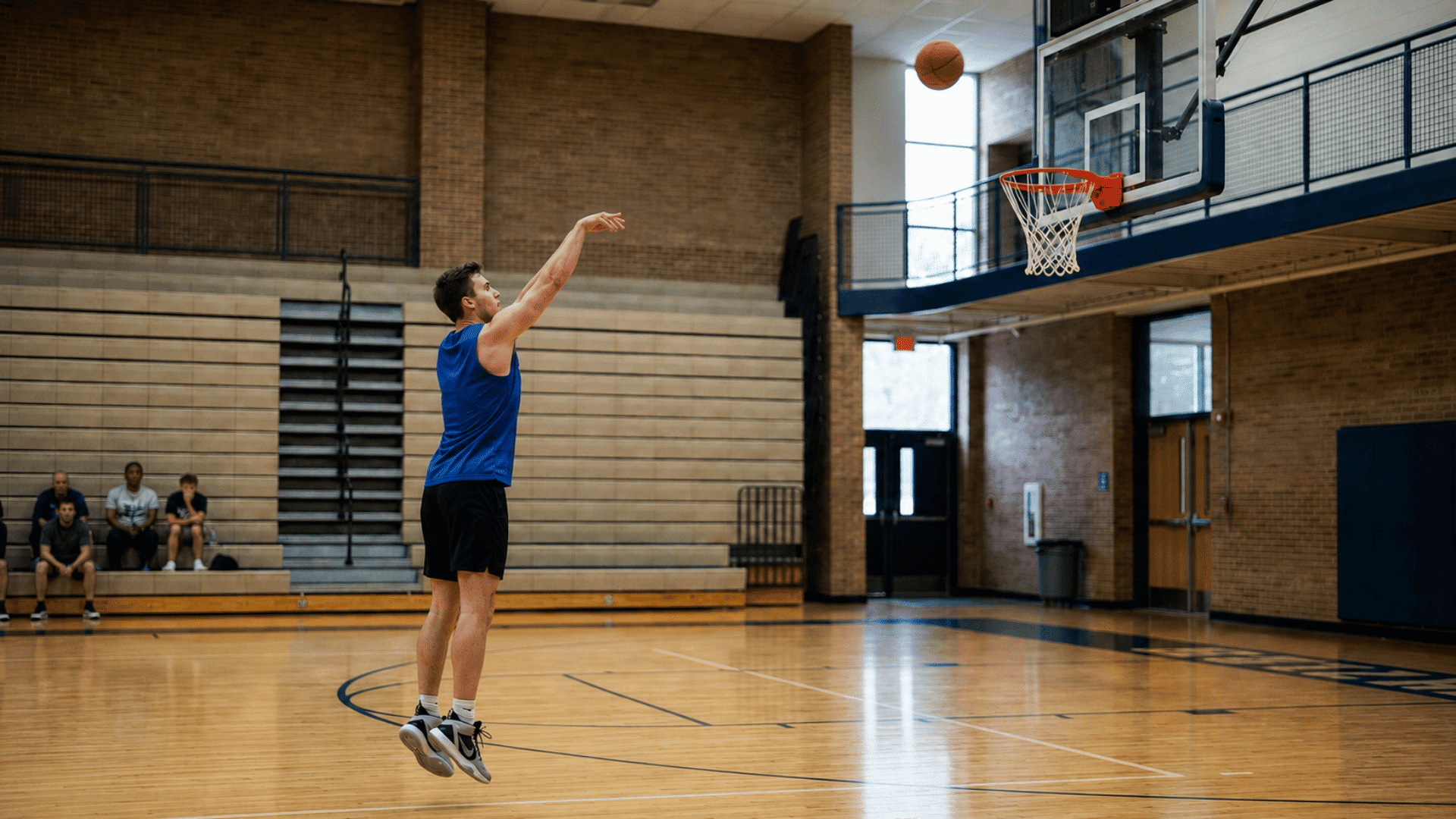 basketball player holding a natural follow through as the ball travels toward the hoop on an indoor court
