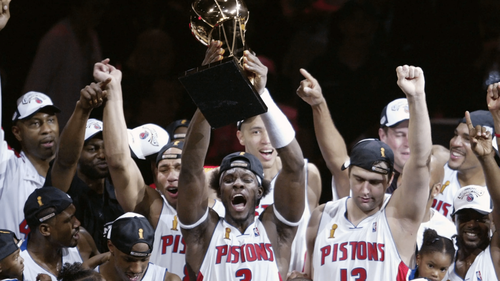 basketball players in pistons jerseys celebrating together while raising a championship trophy above the cheering crowd