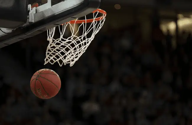 Basketball going through hoop in indoor sports arena with blurred spectators in background