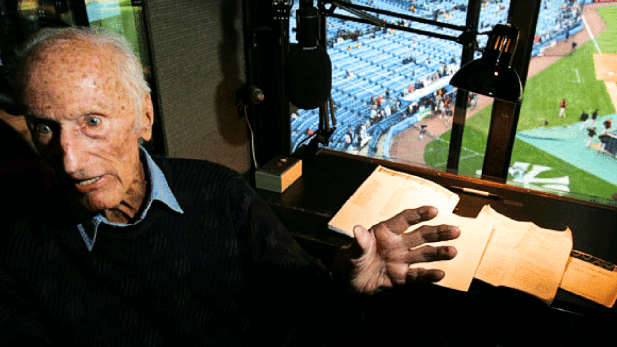 bob sheppard inside yankee stadium press box preparing announcements with microphone notes and baseball field in view