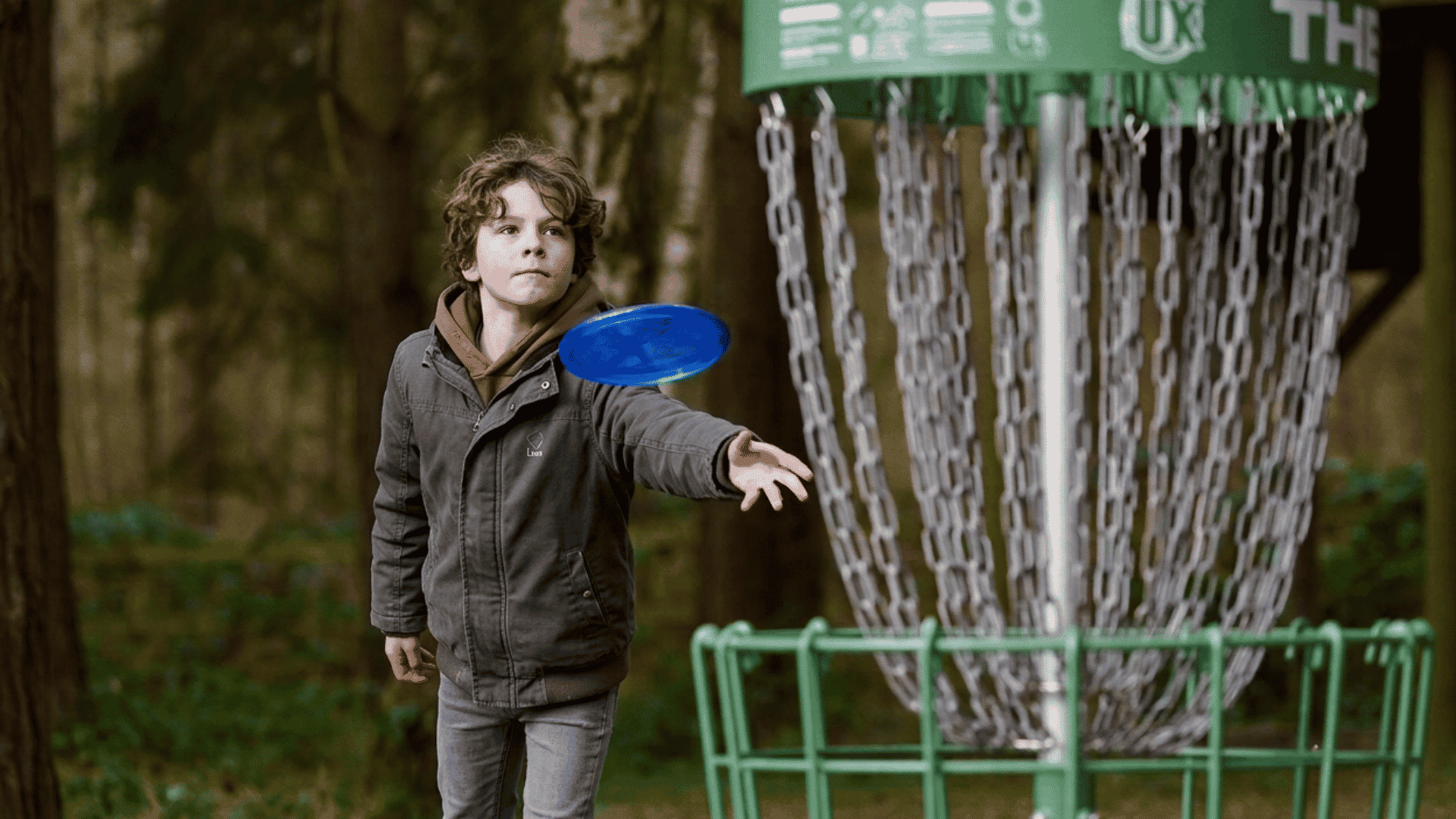 Child throwing a blue disc toward a disc golf basket in a wooded park