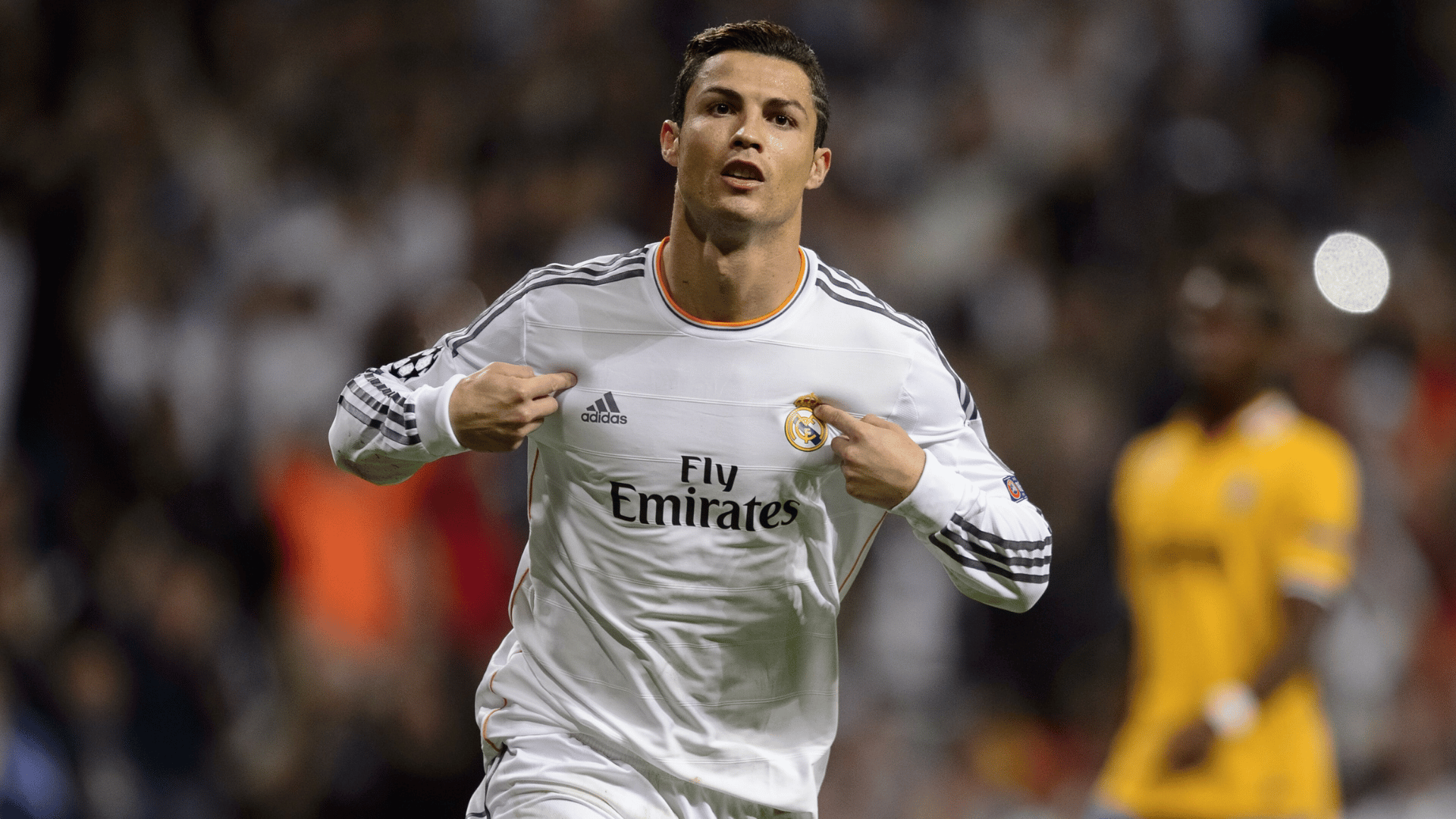 cristiano ronaldo wearing a white club jersey pointing at the team badge during a stadium match