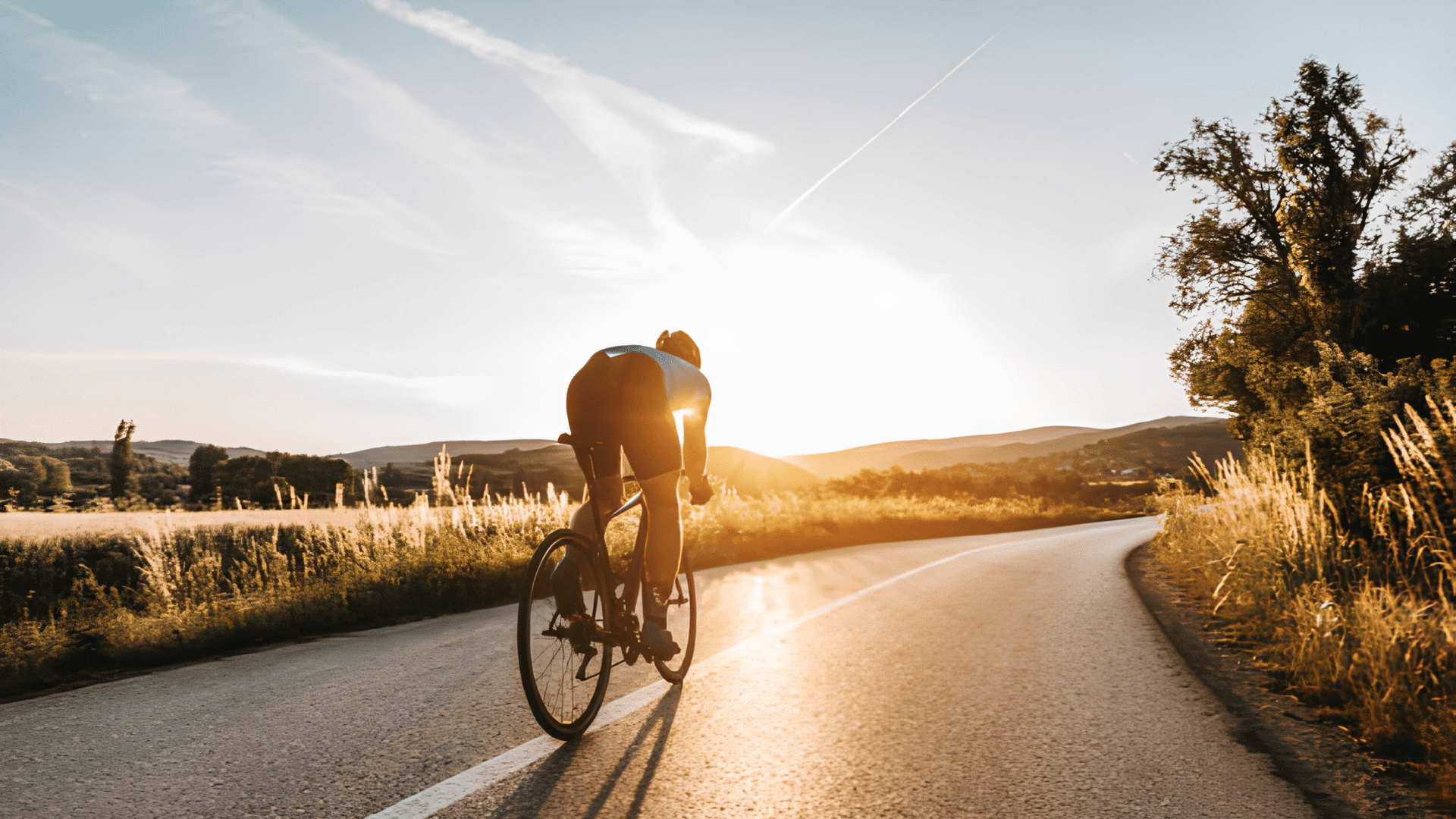 cyclist riding a road bike along a quiet country road during sunset with golden light across the landscape